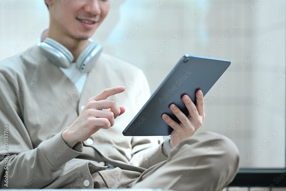 Casual young asian man with headphone around neck using digital tablet at office Casual young asian man with headphone around neck using digital tablet at office