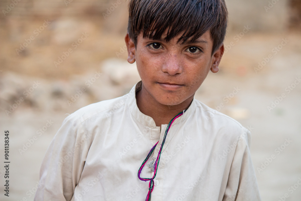 A young boy with dark hair and a serious expression, wearing a light shirt, sits outdoors A young boy with dark hair and a serious expression, wearing a light shirt, sits outdoors
