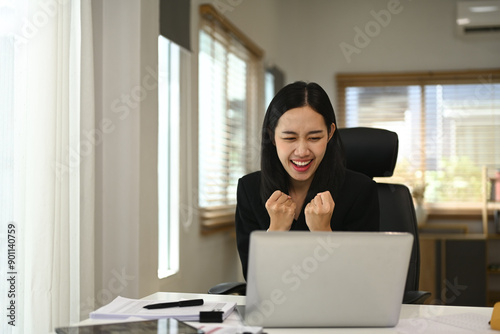 Excited young businesswoman celebrating her achievement while reading good news on laptop