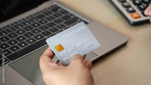 A person is holding a credit card in front of a laptop. Shopping Online Holding Credit Card Making Payment, financial responsibility and the importance of managing one's finances