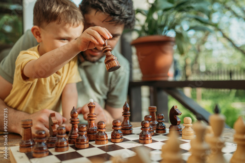 Son playing chess with father on porch photo