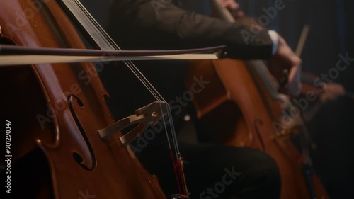Cropped shot of virtuous string orchestra playing bass, cello and violin while giving live concert on dark stage