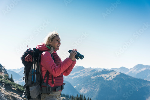 Happy mature woman with backpack holding binocular on mountain photo