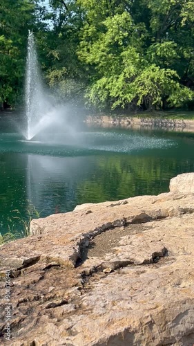 Erupting pond fountain trees boulders reflections daytime natural landscape
