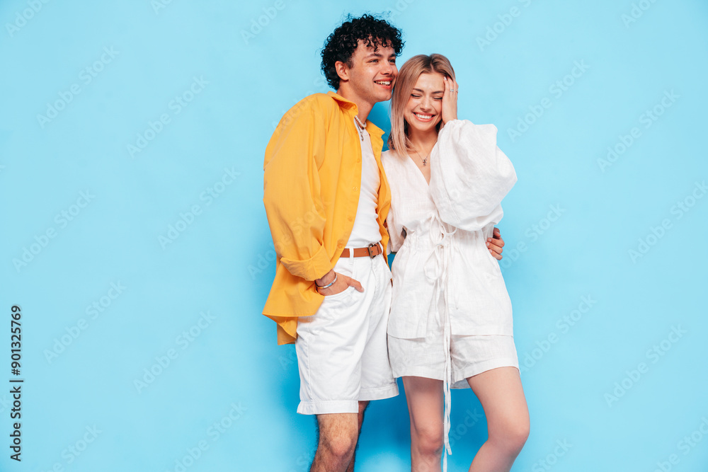 Happy beautiful romantic teenage couple. Smiling handsome caucasian man and young woman in summer clothes posing in studio, hugging sharing emotions, cheerful and happy. Isolated on blue