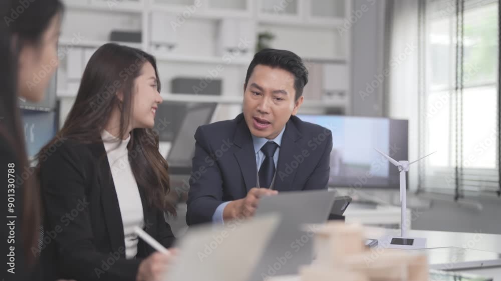 Businesspeople and real estate developers are in a meeting to plan urban and building design for a new project. Team are discussing at desks with computers displaying their work and building plans.