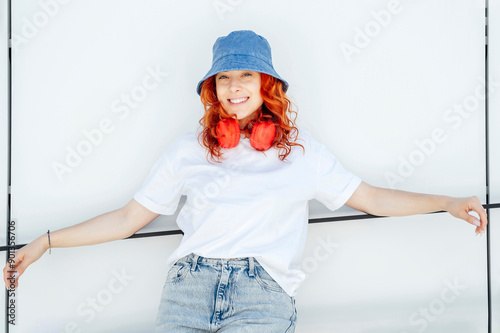 Smiling woman wearing bucket hat leaning on white wall
