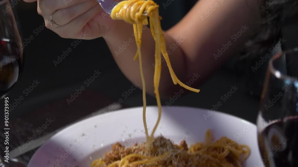 Slow motion of fork scooping spaghetti served on white plate. Pasta rolled on fork.