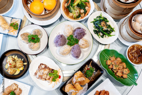 Fototapeta Naklejka Na Ścianę i Meble -  Image of various Chinese dim sum in a bamboo steamer, equipped with chopsticks and tea, on a wooden table. 