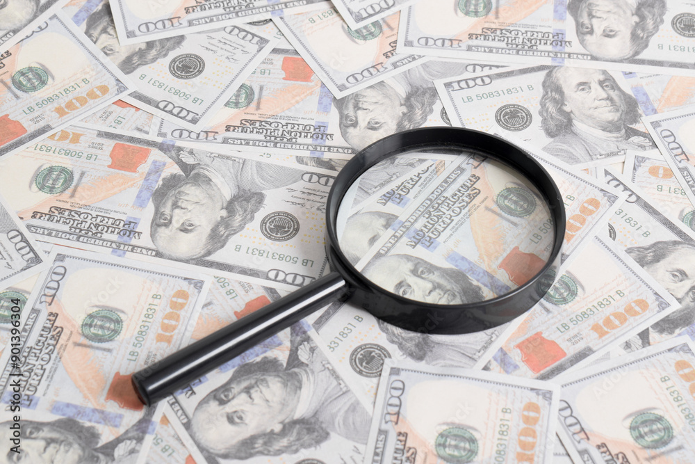 Magnifying glass on the background of a bundle of dollars on the table. Texture US dollars. Banknotes. American money Magnifying glass on the background of a bundle of dollars on the table. Texture US dollars. Banknotes. American money