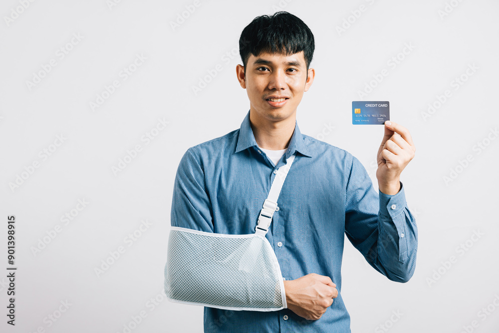 A man confidently smiles with broken arm in a support splint, managing medical bills through a credit card payment. Happy Asian man in a sling white background, highlighting health care accessibility. A man confidently smiles with broken arm in a support splint, managing medical bills through a credit card payment. Happy Asian man in a sling white background, highlighting health care accessibility.