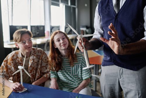 Selective focus shot of unrecognizable teacher holding wind turbine model telling teenagers about renewable energy photo