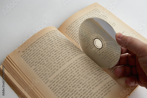 A hand holding a CD between the pages of an open book with text, English language learning, educational courses, self-study photo