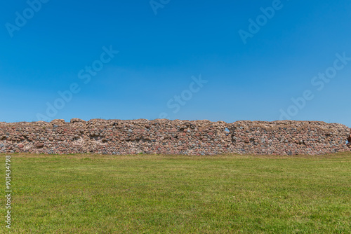 three stripes - green grass, a medieval castle wall made of stones and bricks, blue sky.