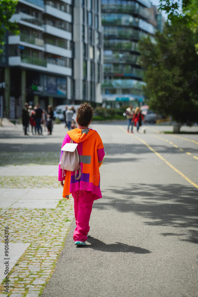 Girl in bright orange clothes and with a backpack walks along city street Girl in bright orange clothes and with a backpack walks along city street
