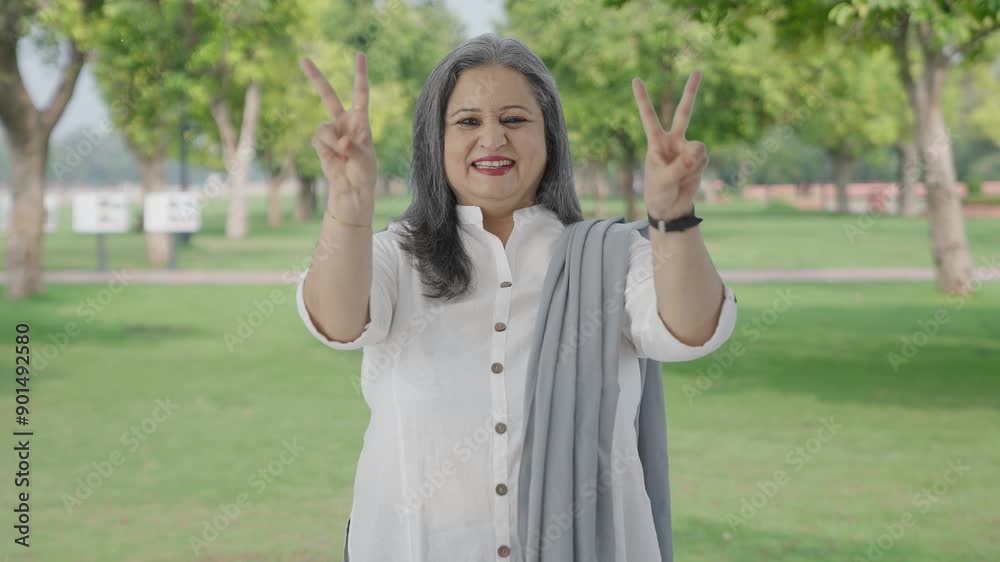 Happy Indian mother showing victory sign in park Happy Indian mother showing victory sign in park