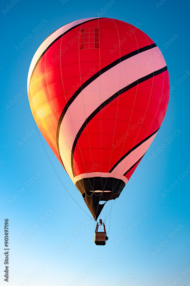 Fototapeta premium A vibrant hot air balloon with a striking red and black pattern set against a clear blue sky background, symbolizing adventure and freedom