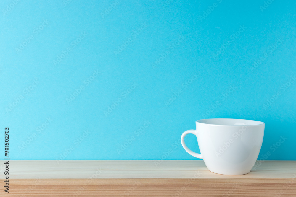 White cup on wooden table over blue background. Coffee concept. White cup on wooden table over blue background. Coffee concept.