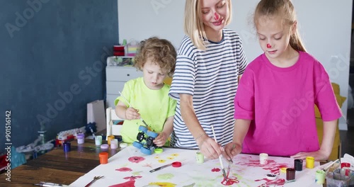 Mom and daughter use red paint to draw large flower on sheet of paper. Girl watches intently as mother uses paintbrush to form petals