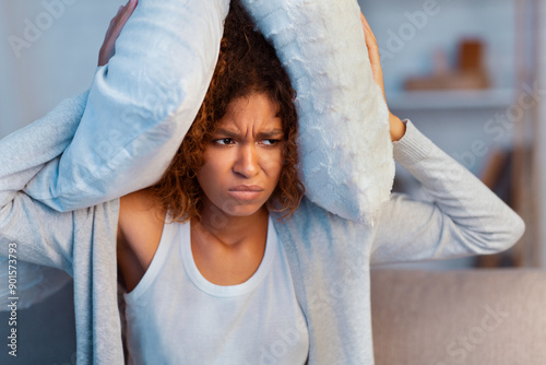 Fotografia Annoyed woman covering ears with pillow, suffering from noisy neighbours