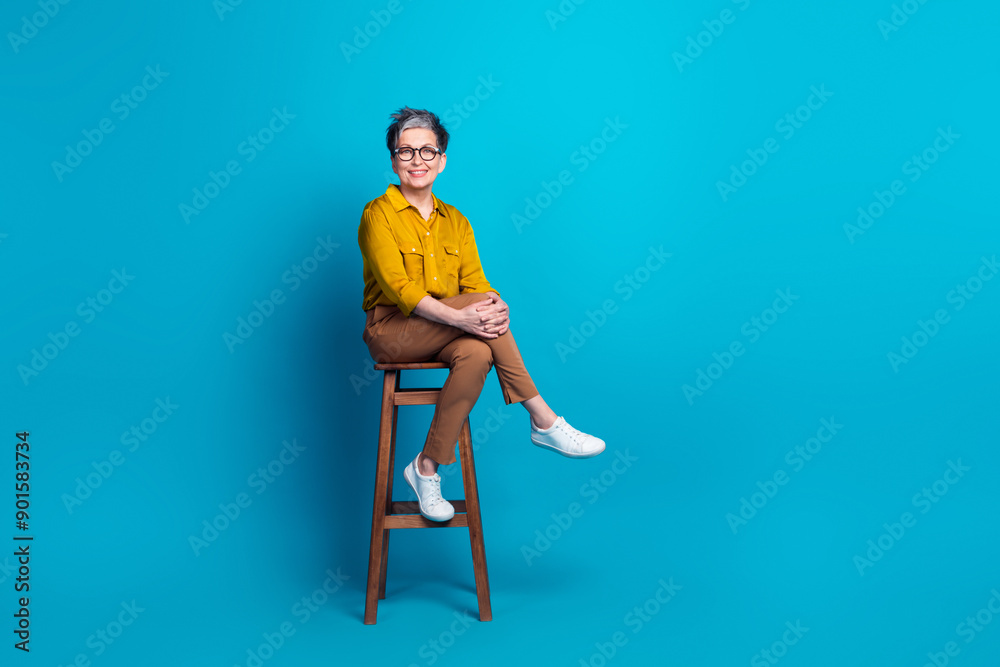 Fototapeta premium Full length photo of pretty cheerful woman wear shirt spectacles sitting chair emtpy space isolated blue color background