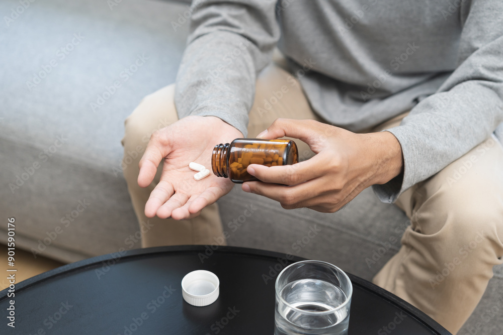 Sick asian young man, male holding tablet pill on hand, painkiller medicine from fever, stomach pain, headache for treatment, take drug or vitamin with glass of water on at home. Health care concept. Sick asian young man, male holding tablet pill on hand, painkiller medicine from fever, stomach pain, headache for treatment, take drug or vitamin with glass of water on at home. Health care concept.