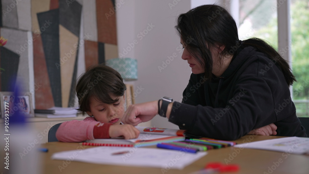 Young boy attentively working on homework while mother provides guidance, colorful pencils and educational materials on the table, illustrating supportive parenting and early education Young boy attentively working on homework while mother provides guidance, colorful pencils and educational materials on the table, illustrating supportive parenting and early education