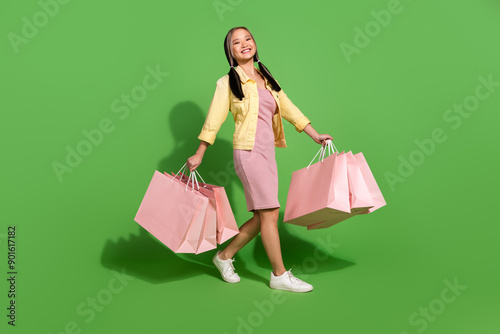 Full body portrait of pretty young woman hold bags walk wear jacket dress isolated on green color background