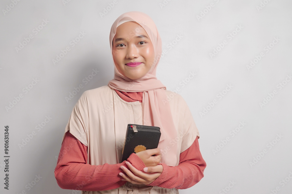 Young Woman in Hijab Holding a Quran Against White Background Young Woman in Hijab Holding a Quran Against White Background