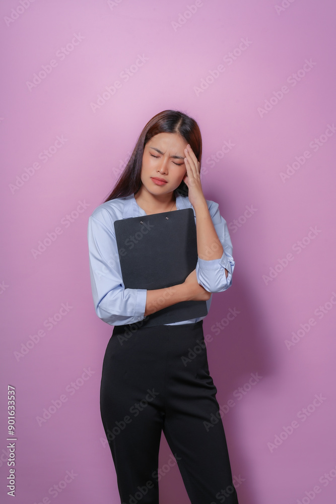 Young businesswoman is holding a clipboard and having a headache while standing on a purple background Young businesswoman is holding a clipboard and having a headache while standing on a purple background