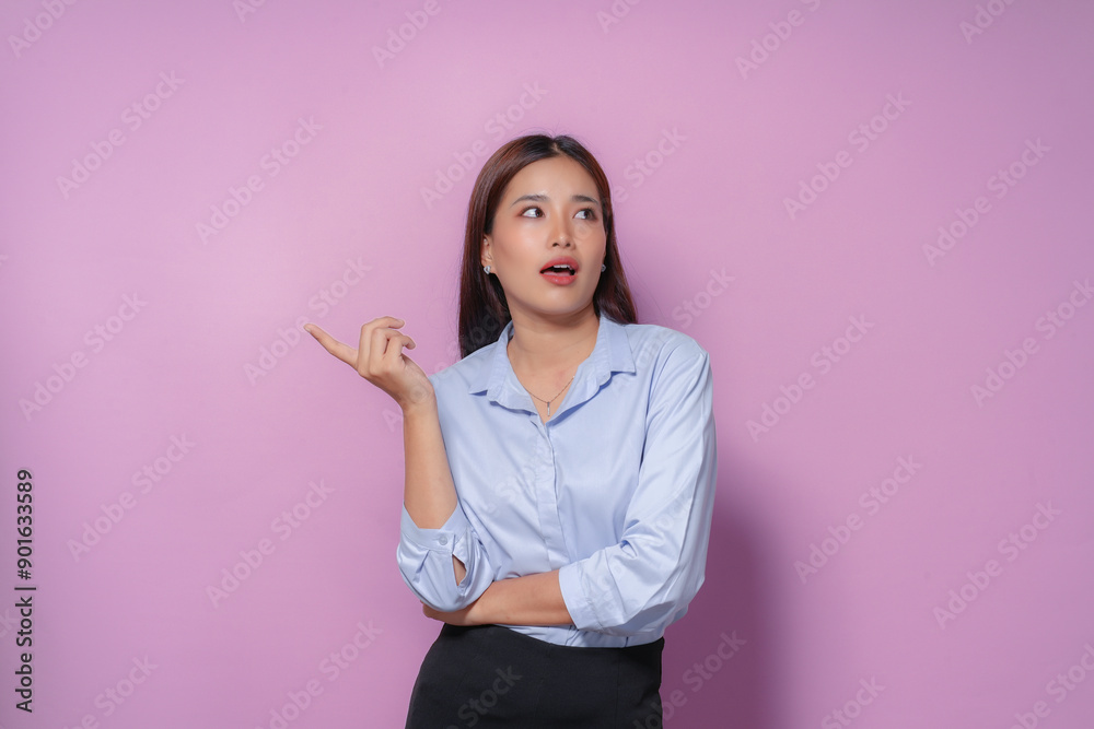 Young asian businesswoman in blue shirt pointing with finger aside giving suggestion on purple background Young asian businesswoman in blue shirt pointing with finger aside giving suggestion on purple background