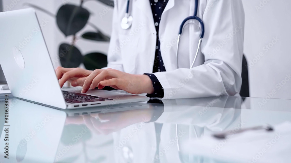 Doctor woman is typing on laptop computer at glass table in clinic, horizontal view. Medicine and pharmacy concept Doctor woman is typing on laptop computer at glass table in clinic, horizontal view. Medicine and pharmacy concept