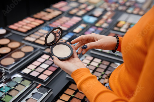 Woman holding face blush in her hands. Colorful eye shadows palettes and other male up products on background photo