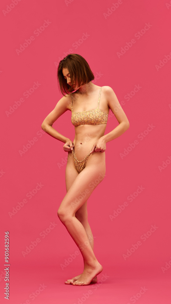 Fototapeta premium Full-length image of attractive young women with slim body, posing swimsuit against pink studio background. Wellness. Concept of female beauty, body and health care, sport and diet