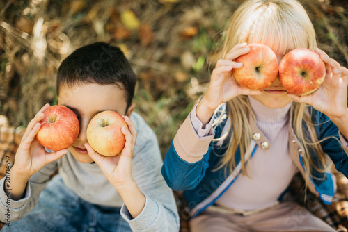 Children with Apple in Orchard. Harvest Concept. Garden, boy and blonde girl eating fruits at fall. Child picking apples on farm in autumn. Healthy nutrition Garden Food.