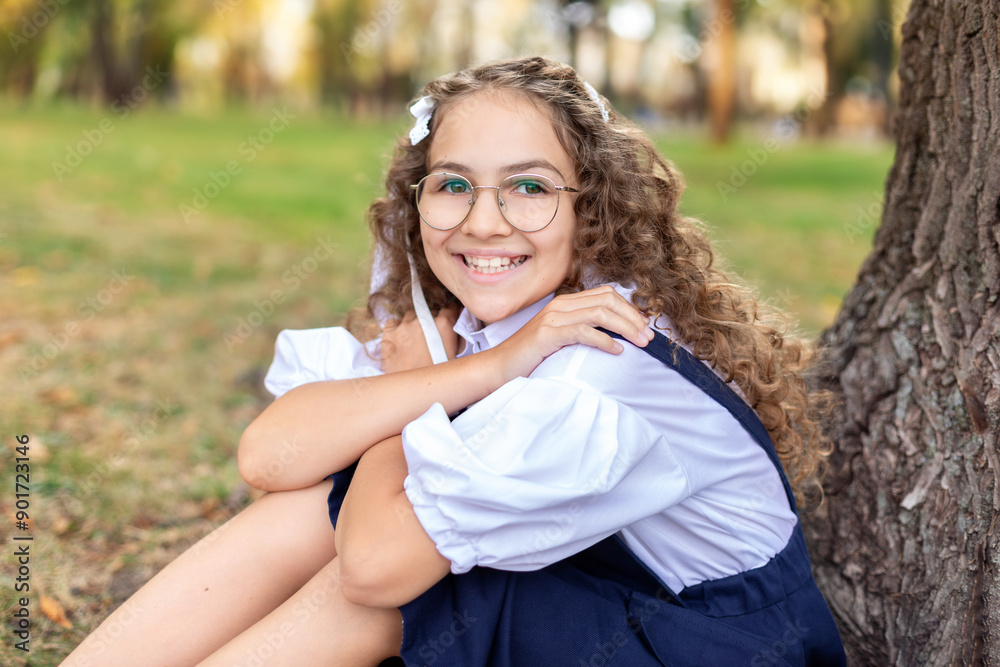 Portrait of cheerful student child girl with curly hair in glasses. Smiling Beautiful Little girl in glasses and in a school uniform sitting on grass in park near the school. Back to school.
Portrait of cheerful student child girl with curly hair in glasses. Smiling Beautiful Little girl in glasses and in a school uniform sitting on grass in park near the school. Back to school.