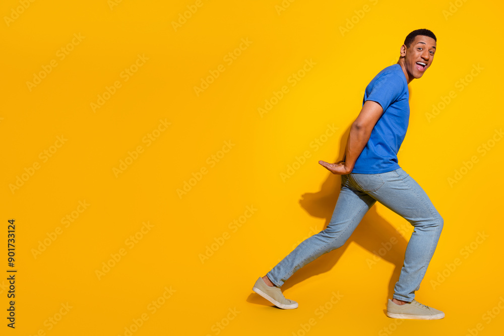 Full size photo of pretty young male hold carry back empty space walk wear trendy blue outfit isolated on yellow color background Full size photo of pretty young male hold carry back empty space walk wear trendy blue outfit isolated on yellow color background