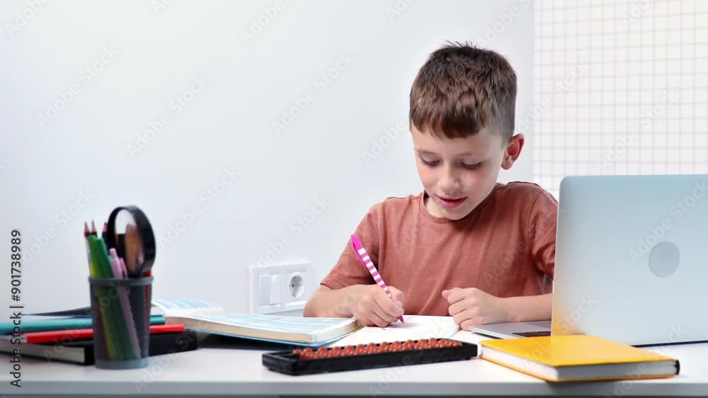 Cute pupil boy studying at home writing in exercise book doing homework, learning at home table Cute pupil boy studying at home writing in exercise book doing homework, learning at home table