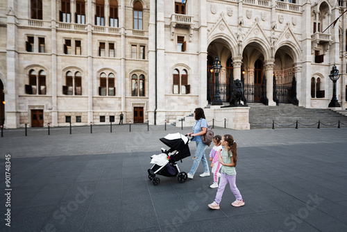 Canvas Print Mother with children walking near historic building in city square in Budapest,