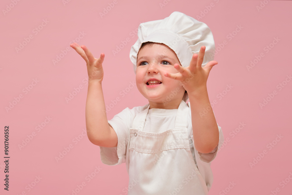 Child dressed in a white cook's uniform stands in front of a pink background, looking very excited. Kid aged 3 years (three year old boy) Child dressed in a white cook's uniform stands in front of a pink background, looking very excited. Kid aged 3 years (three year old boy)