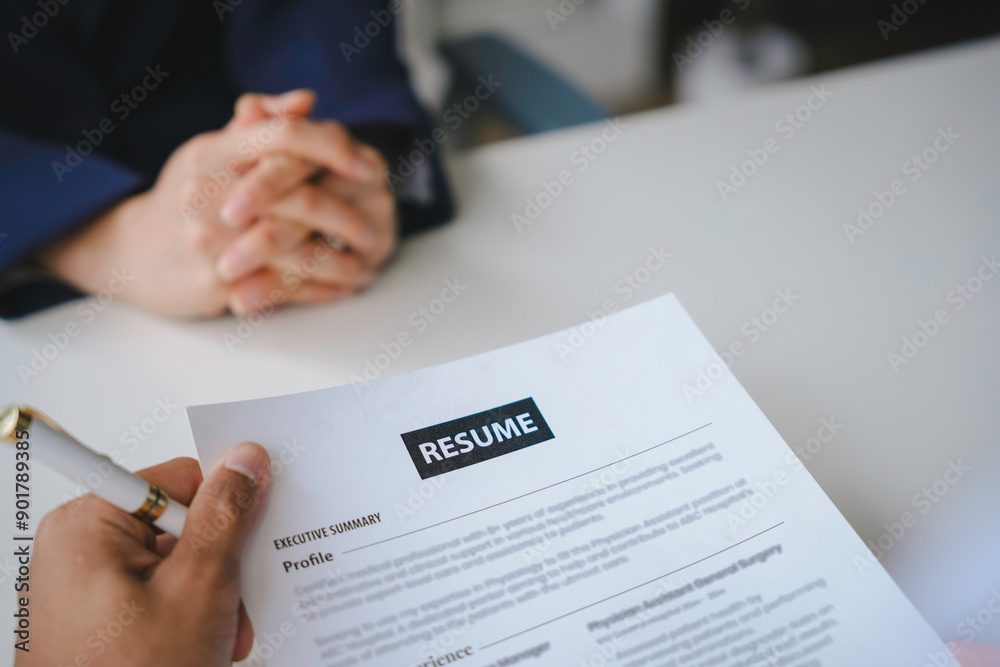 Recruiter is holding a resume, carefully reviewing the applicant's qualifications during a job interview Recruiter is holding a resume, carefully reviewing the applicant's qualifications during a job interview