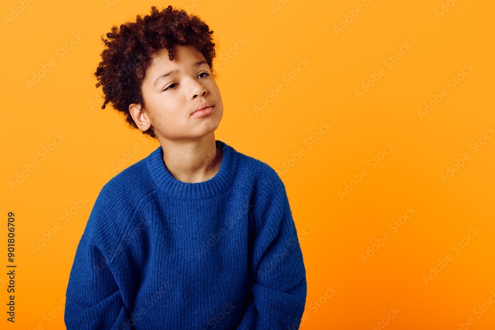 Curious young african american boy in blue sweater gazes upward against a bright orange background, capturing wonder and imagination Curious young african american boy in blue sweater gazes upward against a bright orange background, capturing wonder and imagination