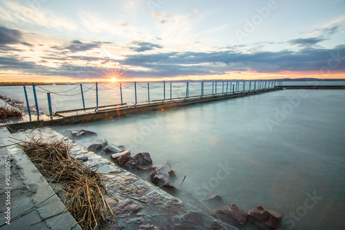 Water landscape taken from the shore of a calm lake. View over the reflecting water to the horizon in the sunset. a jetty or pier at Siofok harbor, Balaton, Hungary photo