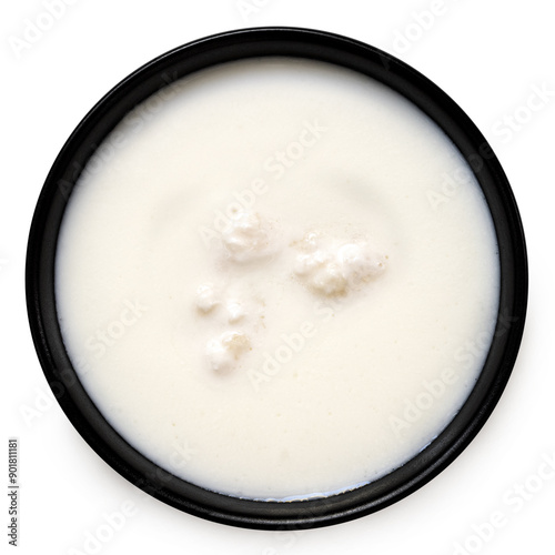 Milk with kefir grains in a black ceramic bowl isolated on white from above. photo