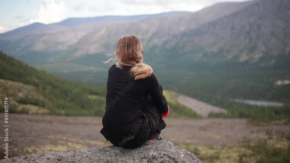 A young woman sits on a rock and admires the mountain valley A young woman sits on a rock and admires the mountain valley