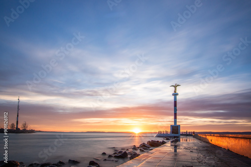 a small marina on a lake. Breakwater and pillar with golden figure in the dreamy sunset. Landscape shot in Siófok, Balaton, Hungary photo