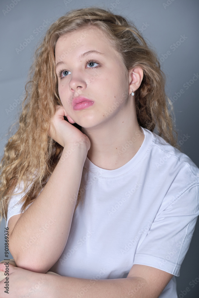Seated with a thoughtful expression, a young woman in a white t-shirt and beige pants poses against a neutral background. The scene emphasizes natural beauty and minimalist style. Seated with a thoughtful expression, a young woman in a white t-shirt and beige pants poses against a neutral background. The scene emphasizes natural beauty and minimalist style.