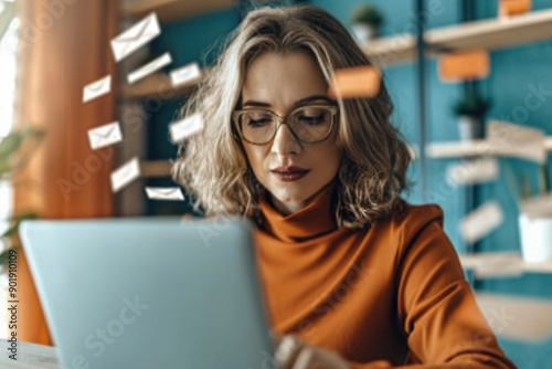 Focused businesswoman working on laptop with flying emails in modern office