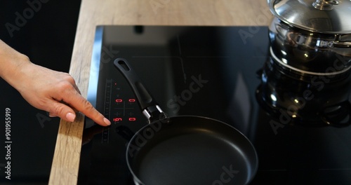 Female hand turn on black induction or electrical cooktop with pans. Comfortable kitchen equipped with modern convenient cooking device. High quality 4k footage photo