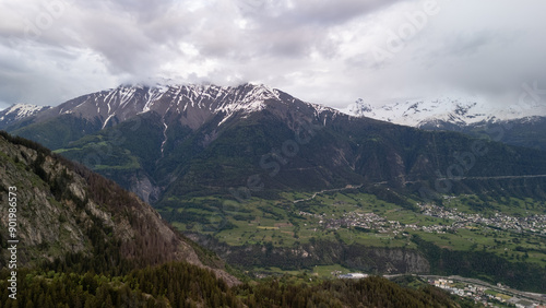 Snow-Capped Mountains Towering Over Verdant Valley Under Cloudy Sky in Spring